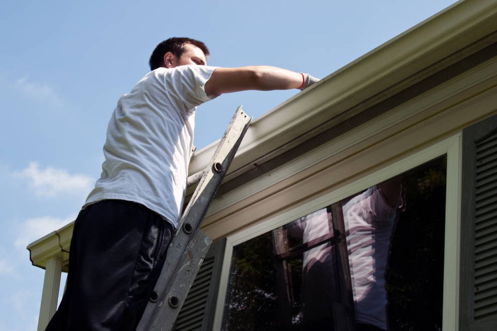 Young man on latter cleaning house gutters